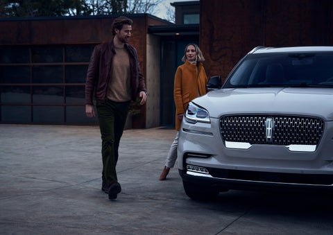 A man and a woman approaching a 2024 Lincoln Aviator® SUV, which illuminates certain lights when they are close | Sheehy Lincoln of Gaithersburg in Gaithersburg MD