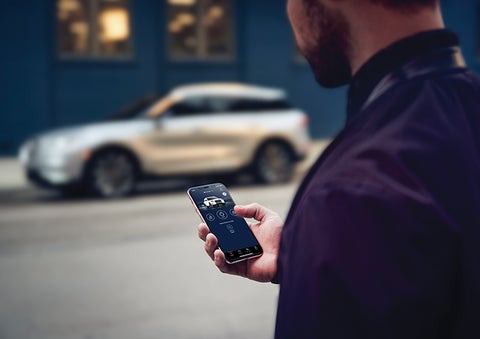 A person is shown interacting with a smartphone to connect to a Lincoln vehicle across the street. | Sheehy Lincoln of Gaithersburg in Gaithersburg MD