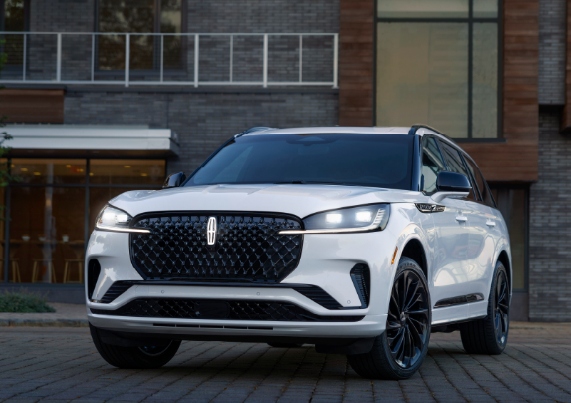 A white 2025 Lincoln Aviator® SUV is shown parked outside a modern building with gray brick and wood accents. | Sheehy Lincoln of Gaithersburg in Gaithersburg MD