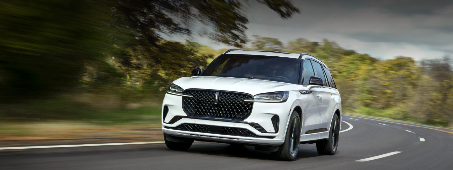 A white 2025 Lincoln Aviator® SUV is being driven down a road lined with trees. | Sheehy Lincoln of Gaithersburg in Gaithersburg MD
