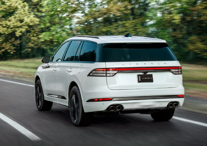 A white 2026 Lincoln Aviator® SUV is being driven away down a road lined with colorful trees. | Sheehy Lincoln of Gaithersburg in Gaithersburg MD
