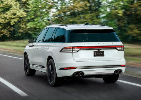 A white 2026 Lincoln Aviator® SUV is being driven away down a road lined with colorful trees. | Sheehy Lincoln of Gaithersburg in Gaithersburg MD