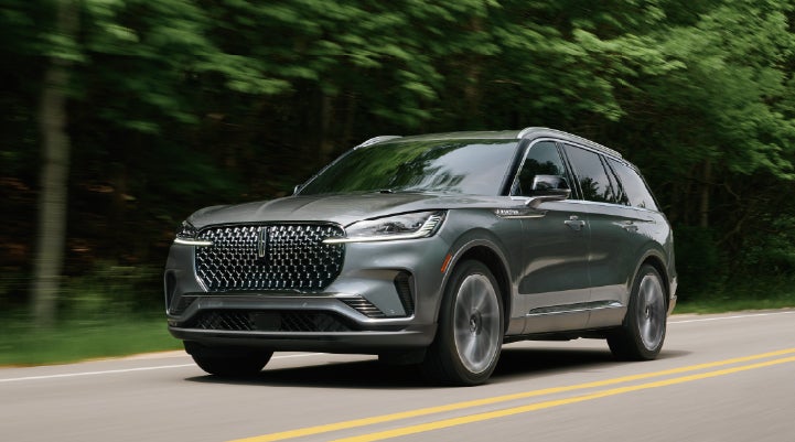 A 2027 Lincoln Aviator® SUV is being driven down a road lined with trees. | Sheehy Lincoln of Gaithersburg in Gaithersburg MD